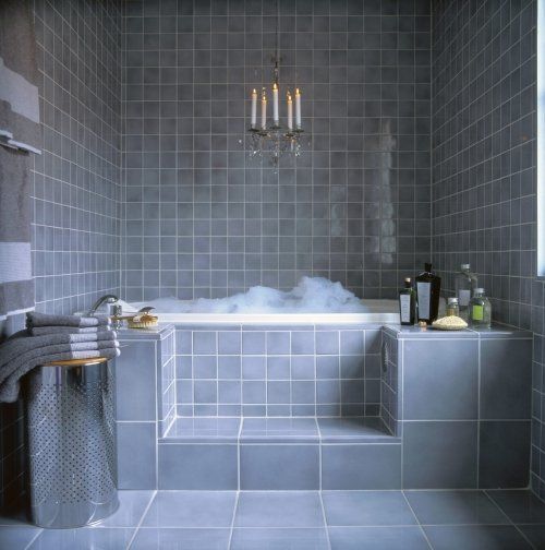 Badekar med grå fliser og dekorativ lysekrone
